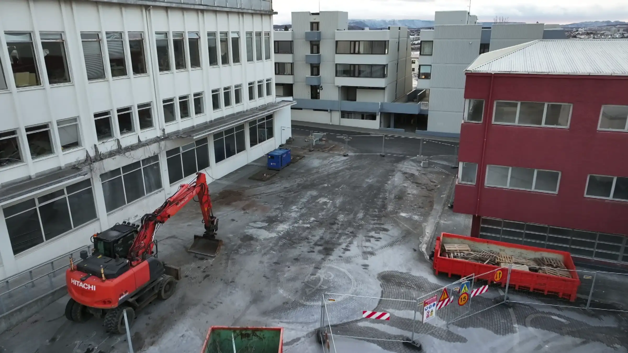 Myndin sýnir til vinstri Fannborg 2 þar sem búið er að rífa part úr þakskyggni byggingarinnar. Á myndinni eru girðingar sem afmarka svæðið og innan þeirra er rauð grafa sem stendur við Fannborg 2